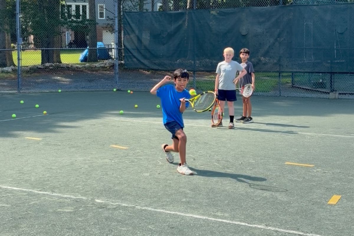 Boy hitting a forehand while other juniors watch during a tennis clinic at Asheboro Racquet & Swim Club