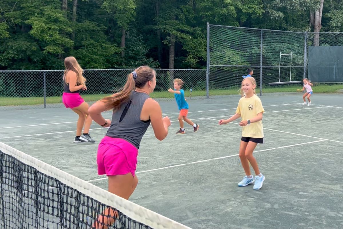 Coach leading young players through footwork drills during a junior tennis clinic at Asheboro Racquet & Swim Club