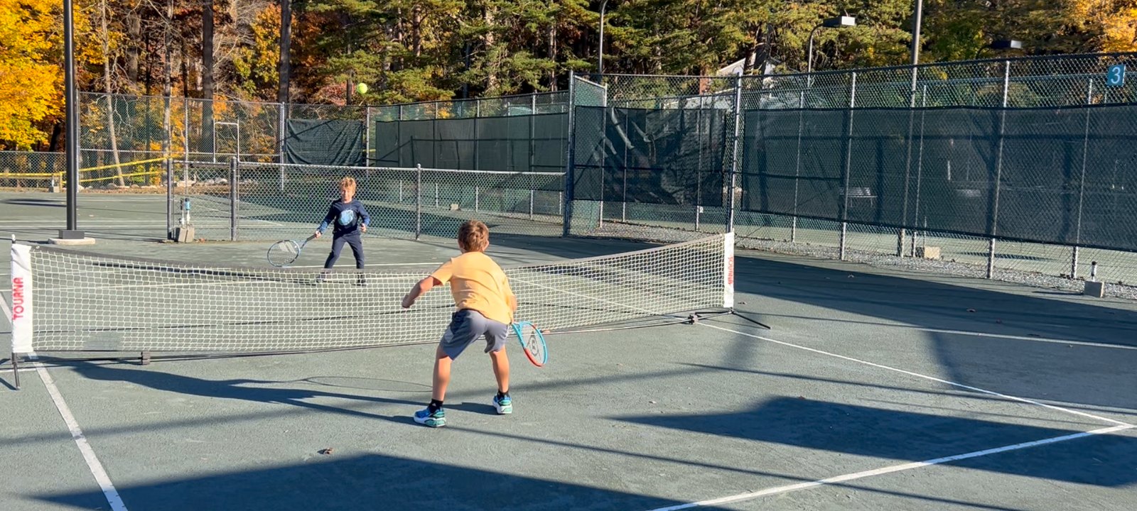 Junior players rallying on a clay court on a bright fall afternoon