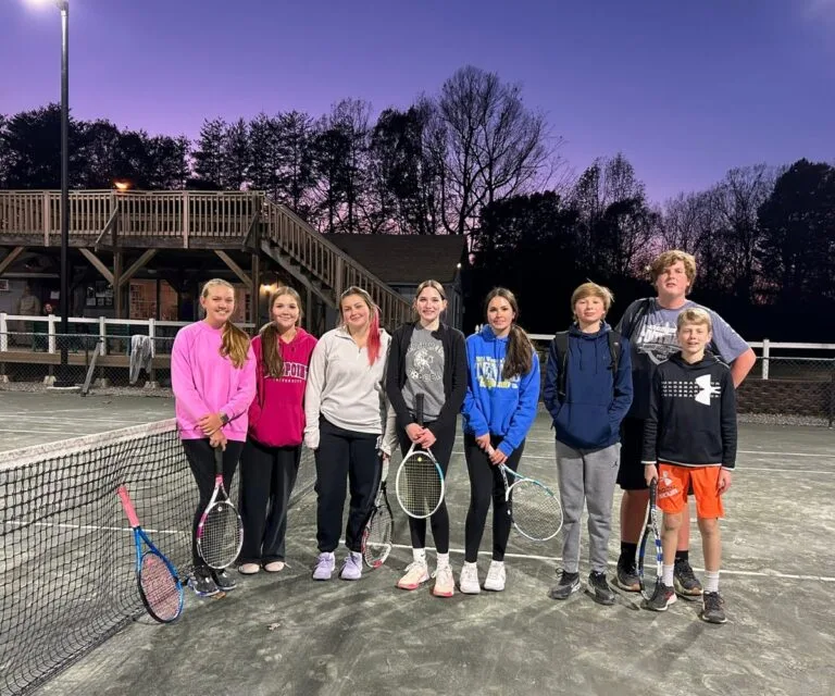 Group of junior tennis players posing with rackets at the net at dusk at Asheboro Racquet & Swim Club