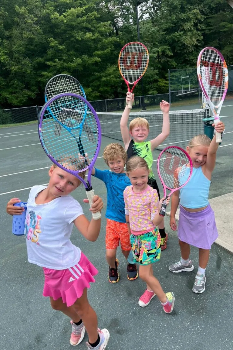 Young children cheering and raising their rackets after a junior tennis clinic at Asheboro Racquet & Swim Club