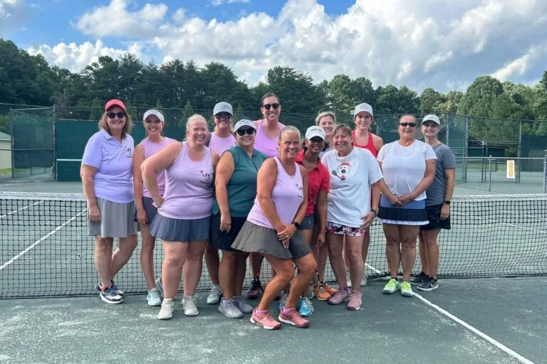 Women's tennis team posing together at the net on the courts at Asheboro Racquet & Swim Club